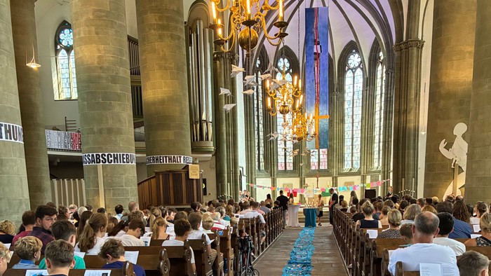 Eine prächtige Kathedrale, gefüllt mit Gläubigen, die in Reihen sitzen, geschmückt mit aufwendigen Verzierungen und Buntglasfenstern.