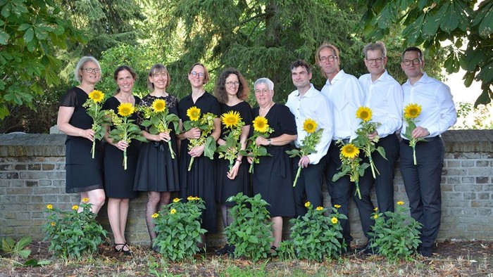 Chormitglieder mit Sonnenblumen in der Hand, links die Frauen in schwarzen Kleidern, rechts die Herren in weißem Hemd und schwarzer Hose.