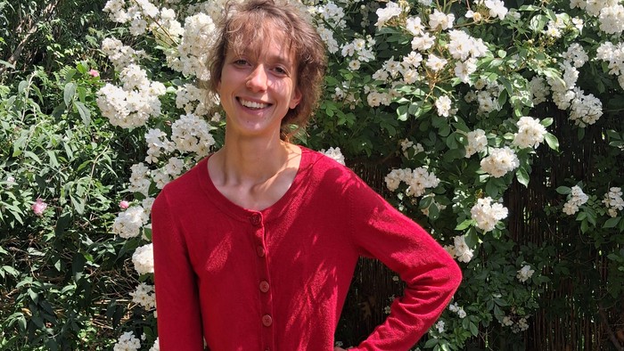Organisten Clara står foran en stor smuk busk med hvide blomster