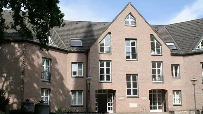 Ein Backsteingebäude mit steilen Satteldächern, großen Fenstern und Fahrrädern, die draußen abgestellt sind.