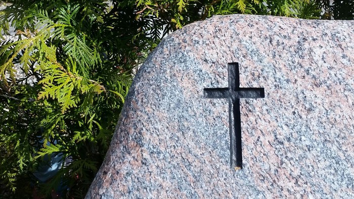En granitsten med en svart korsfesta, omgivet af grønne planter