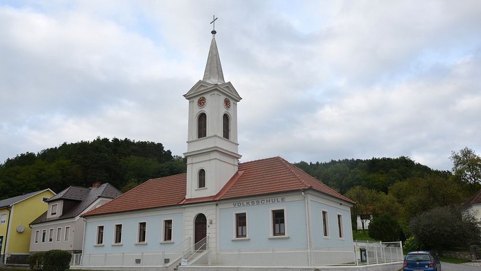 Kleine Kirche mit Uhrturm und rotem Dach in ländlicher Umgebung