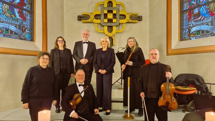 Eine Gruppe von Musiker:innen in formeller Kleidung, die mit Streichinstrumenten in einer Kirche posieren.