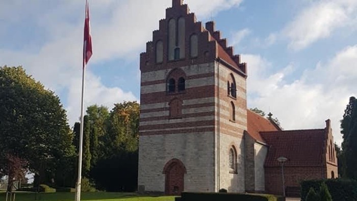 En kvinde går forbi en historisk bygning med tårn og flagstang.