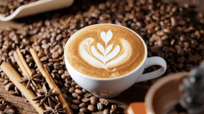 Kunstfærdig latte med hjerte-design på kaffebønner og kanelstænger, der vækker hyggelige aromaer.