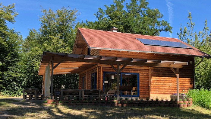Eine rustikale Holzhütte mit überdachter Veranda, Solarpaneelen und von Grün umgeben.