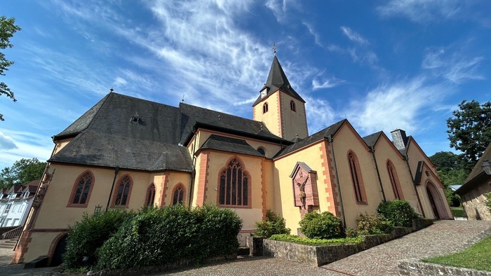 Bezaubernde Kirche mit hohem Kirchturm und hellen Wänden vor einem strahlend blauen Himmel.