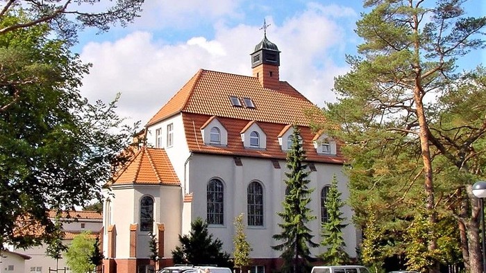 Ein weißes Gebäude mit rotem Dach und Turm, umgeben von Bäumen und Autos.