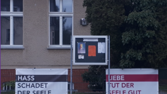 Zwei deutsche Schilder an einer Gebäudewand bilden einen Kontrast zwischen *„Hass schadet der Seele“* und *„Liebe tut der Seele gut“*.