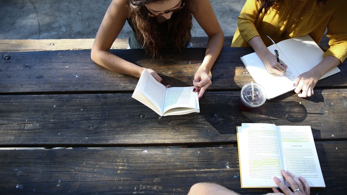 Zwei Frauen sitzen auf einer Holzbank und lesen Bücher.
