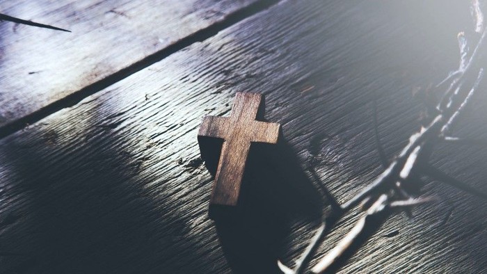 A wooden cross casts a shadow on a textured wooden surface under sunlight.