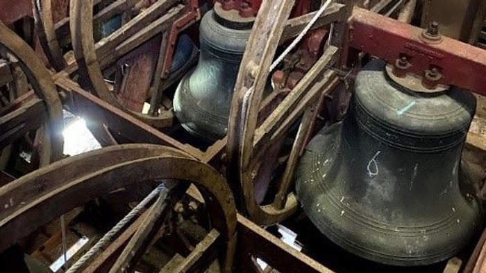 Antique wooden bell mechanism with large hanging bells and pulley wheels in a rustic setting.
