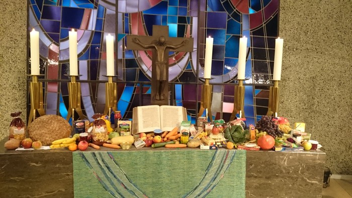 Bunte Altarausstellung mit religiöser Kunst, Kerzen und einer Auswahl an Früchten, Brot und Lebensmitteln.