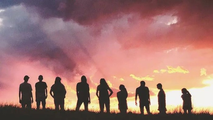 Gruppe von Menschen als Silhouetten vor einem leuchtenden Sonnenuntergangshimmel auf offenem Feld.
