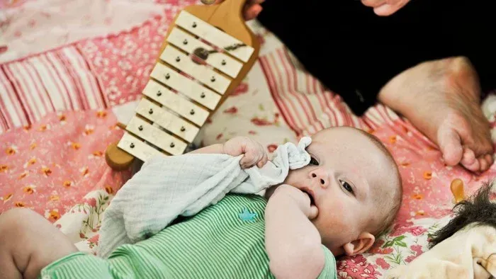 Nysgerrig baby, der leger med et træxylofon, mens den ligger på et farverigt tæppe.