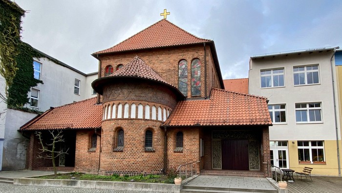 Das Bild zeigt eine rote Backsteinkirche mit spitzem Dach und einem kleinen Turm.