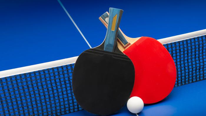 Tischtennisschläger und -ball auf einem blauen Tisch mit Netz platziert.