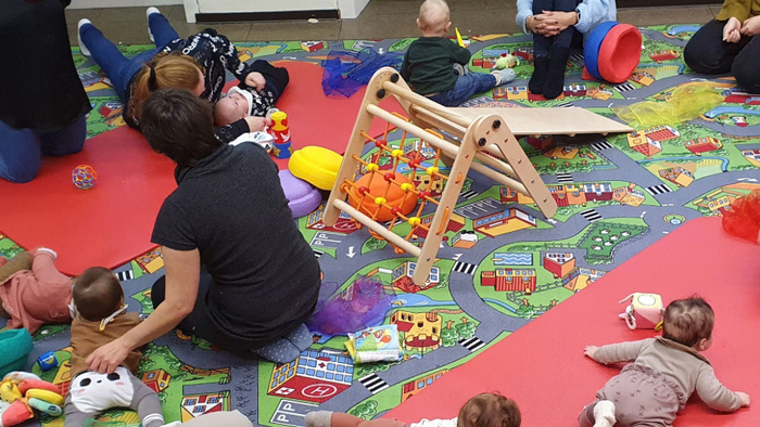 Kinder, die auf einer bunten Spielmatte in einer Gruppe spielen und mit verschiedenen Spielzeugen interagieren.