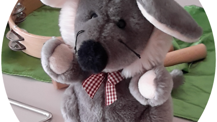 Ein grauer Stofftier-Koala mit roter Schleife sitzt auf einem grünen Tuch.