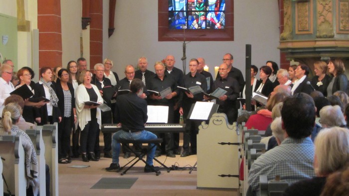 Ein Chor singt in einer Kirche, Zuschauer sitzen auf Bänken