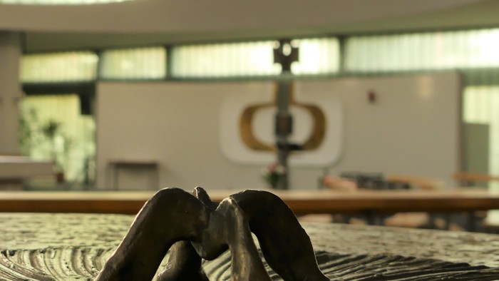Eine schwarze Skulptur einer sitzenden Figur steht auf einem strukturierten, kreisförmigen Boden in einem modernen Innenraum.