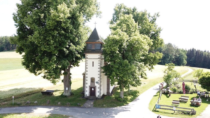 Idyllische weiße Kapelle, umgeben von üppigem Grün und einem gewundenen Landweg.