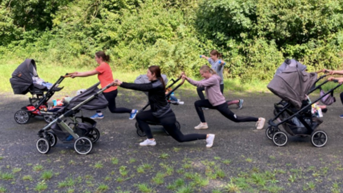 Eine Gruppe von Menschen, die im Freien joggen und dabei Kinderwagen auf einem Parkweg ziehen.