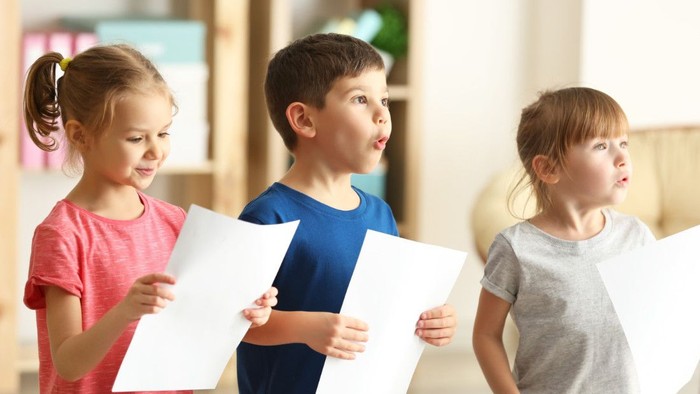 Drei Kinder halten Blätter und singen.