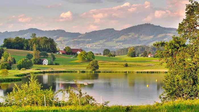 Ruhige Landschaft auf dem Land mit einem stillen See, üppigem Grün und sanften Hügeln unter einem sanften Himmel.