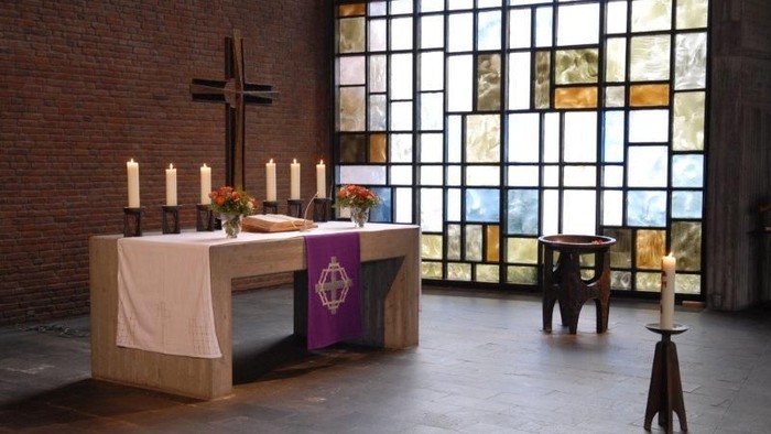 Ein Altar in einer Kirche mit Kerzen, Kreuz und buntem Fenster