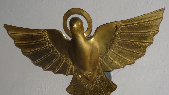Goldenes Metalltauben-Emblem mit ausgebreiteten Flügeln und Heiligenschein, das Frieden symbolisiert.