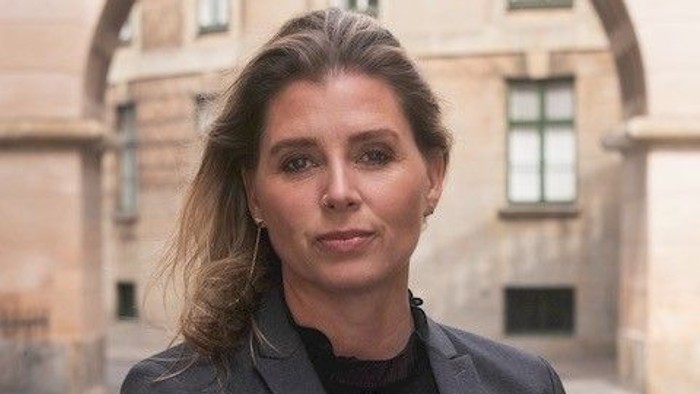 Professionel kvinde i mørk blazer, stående i en buet gårdsplads.