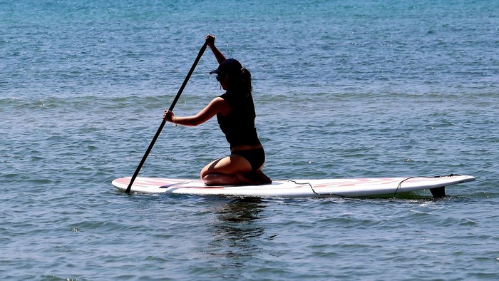 Person, die entspannt auf einem ruhigen, blauen Ozean mit einem langen Paddel Stand-Up-Paddling betreibt.