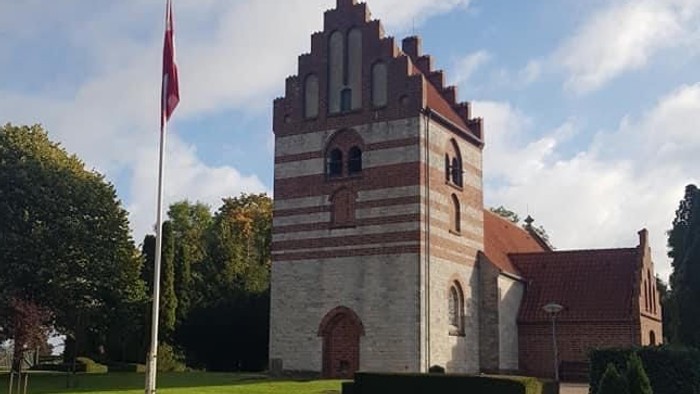 En kvinde går forbi en historisk bygning med tårn og flagstang.