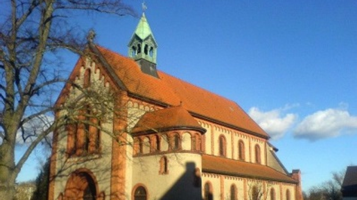 Kirchengebäude mit rotem Dach und grünem Turm im Sonnenlicht