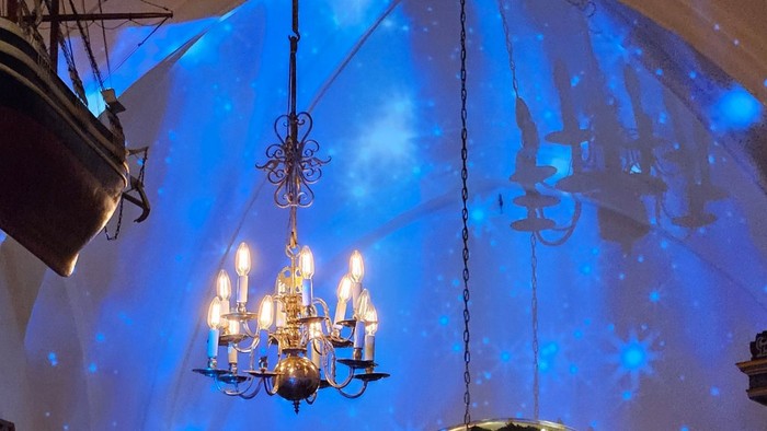 Religiøs ceremoni i en stor, blåoplyst kirke med præster, der synger, og prægtige dekorationer.