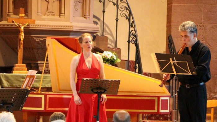 Une soprano chante sur scène dans une église avec des instrumentistes et un public.