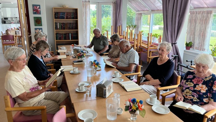 En gruppe pensionister sidder om bordet og spiller bridge i en lys og behagelig lokalitet.