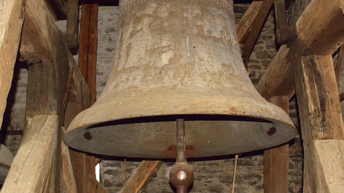 Ein großer, alter Glocke hängt in einem hölzernen Glockenturm.