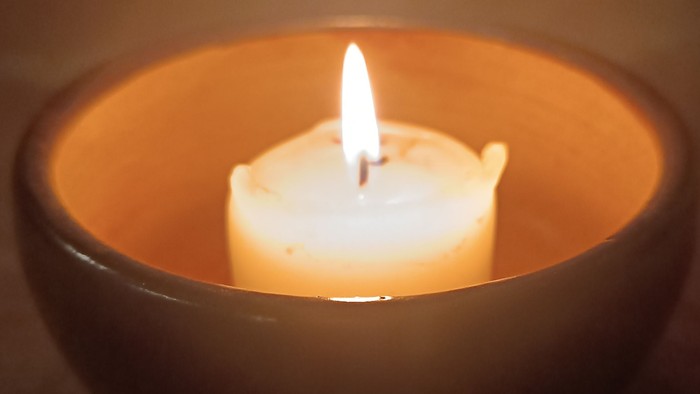 Eine brennende Kerze in einer dunklen, warmtönigen Schale, die sanftes, mildes Licht wirft.