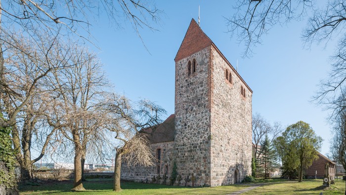 Alte Kirche mit Turm und spärlichem Blattwerk