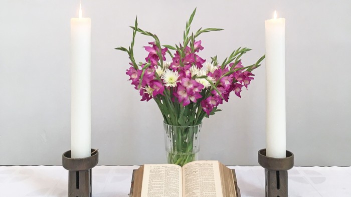 Ein Kreuz, zwei Kerzen, eine Vase mit Blumen und eine offene Bibel auf einem Tisch