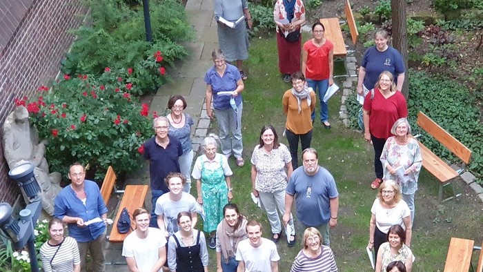 Eine vielfältige Gruppe von Menschen, die sich im Freien in einem Garten für ein Gruppenfoto aufstellen.