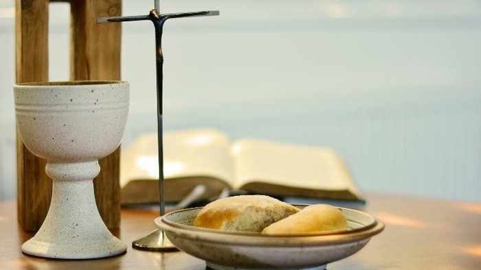 Heilige Kommunionsgegenstände, darunter Kelch, Brot und eine offene Bibel auf einem Holztisch.