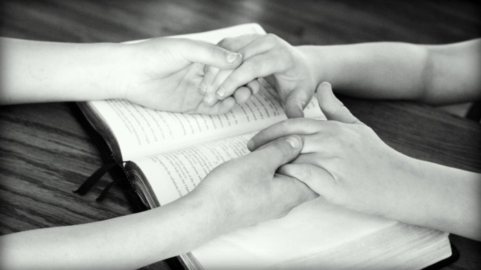 Zwei Hände, die sanft ein offenes Buch halten, während verschränkte Finger darauf ruhen.