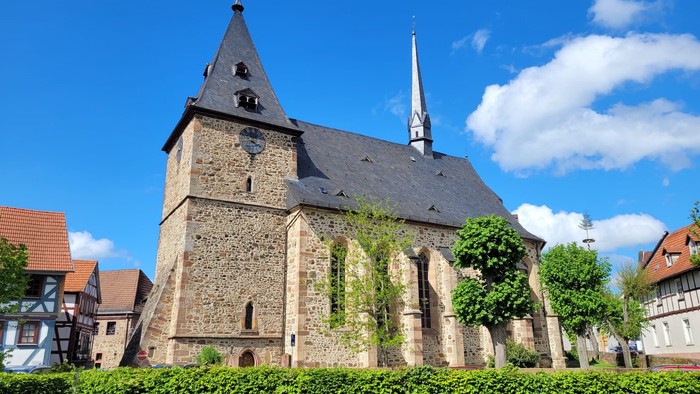 Historische Steinkirche mit steilem Turm und üppigem Grün in einem malerischen europäischen Dorf.