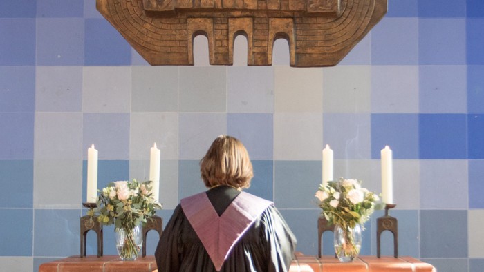 Person in Robe vor Altar mit Kerzen und Statue