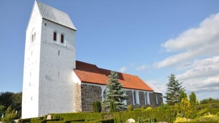 En hvid kirke med tårn og rødt tag i en grøn og træfattig omgivelse