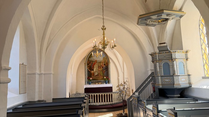 Elegant kirkeinteriør med hvælvede lofter, kirkebænke og prægtige lysekroner, der oplyser alterområdet.