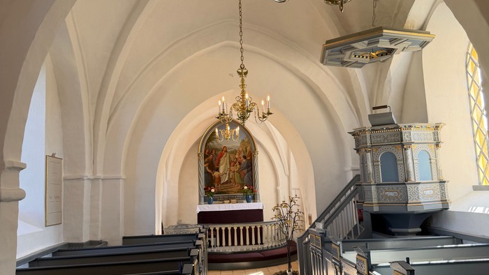 Elegant kirkeinteriør med hvælvede lofter, kirkebænke og prægtige lysekroner, der oplyser alterområdet.